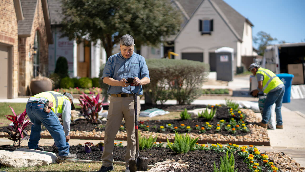 marketing for landscapers - landscaper holding phone and standing on front lawn with workers behind him