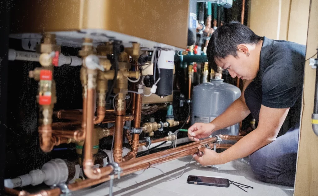 image of plumber repairing a pipe after using plumbing business software