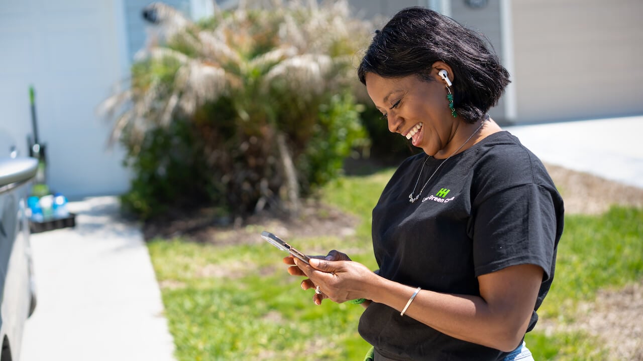 professional carpet cleaner holding phone while standing in front of a home