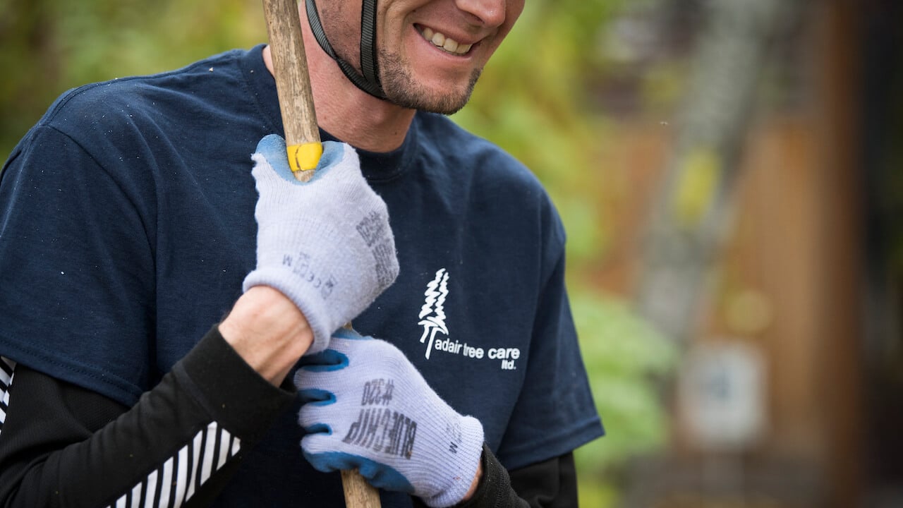 arborist holding equipment and wearing shirt with tree company name