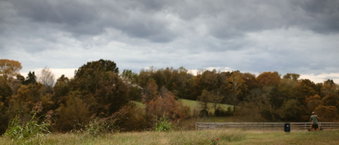 Lanscaper mowing a lawn while storm clouds roll in.