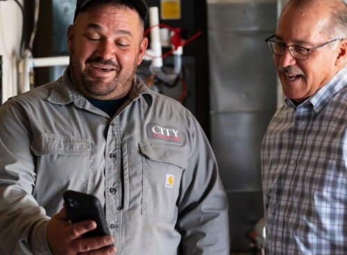 HVAC technician showing something on his phone to a smiling customer.