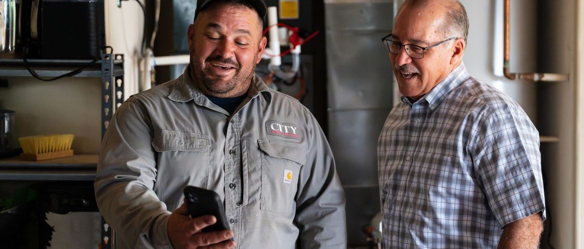 HVAC technician showing something on his phone to a smiling customer.