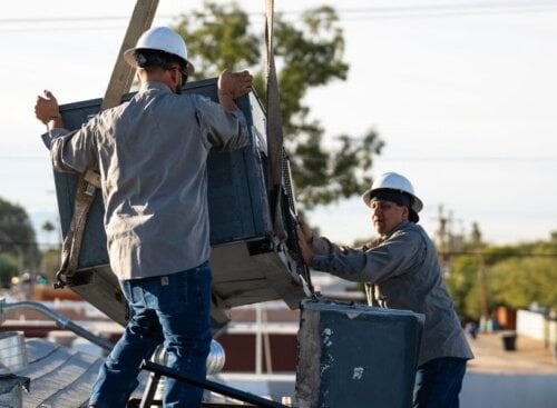 Two HVAC technicians installing an air conditioning unit on a rooftop
