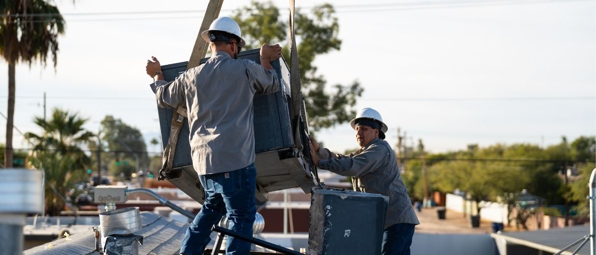 Two HVAC technicians installing an air conditioning unit on a rooftop