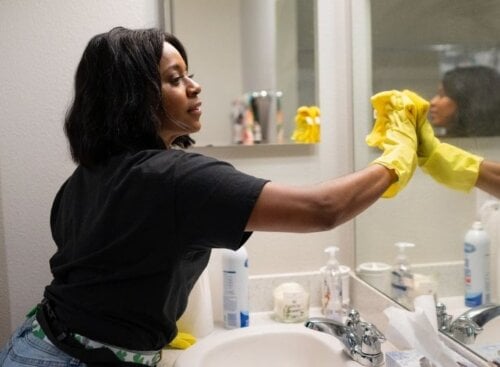 Woman wearing yellow rubber gloves cleaning mirror