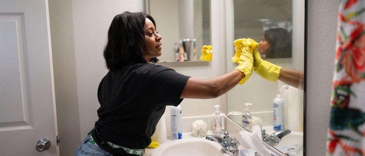 Woman wearing yellow rubber gloves cleaning mirror