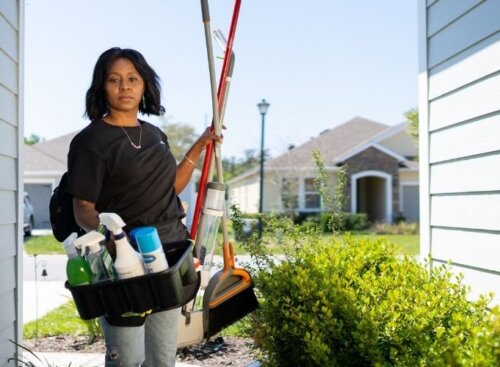 Woman carrying cleaning tools into a resident's house