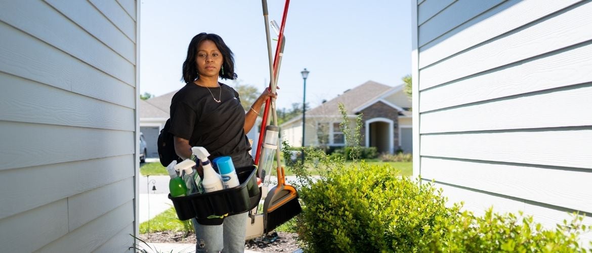 Woman carrying cleaning tools into a resident's house