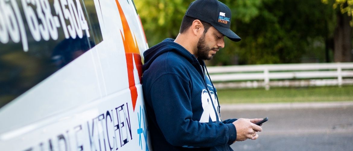 Man leaning against van while looking down at phone