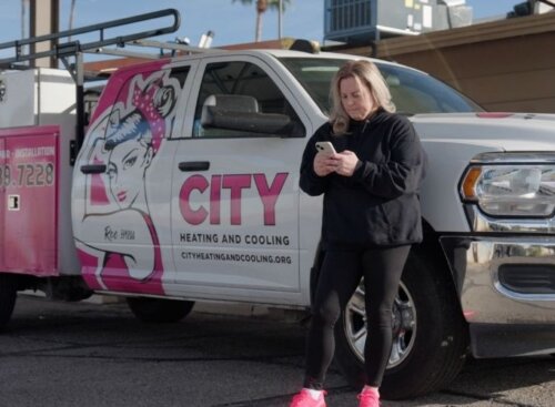 Woman on her phone standing next to a pink and white partial wrapped pickup truck