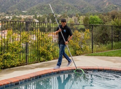 Pool cleaning technician skimming a resident's pool