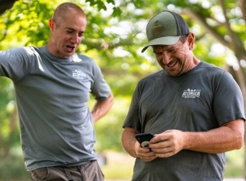 Two landscaping technicians on the job looking down at a mobile device