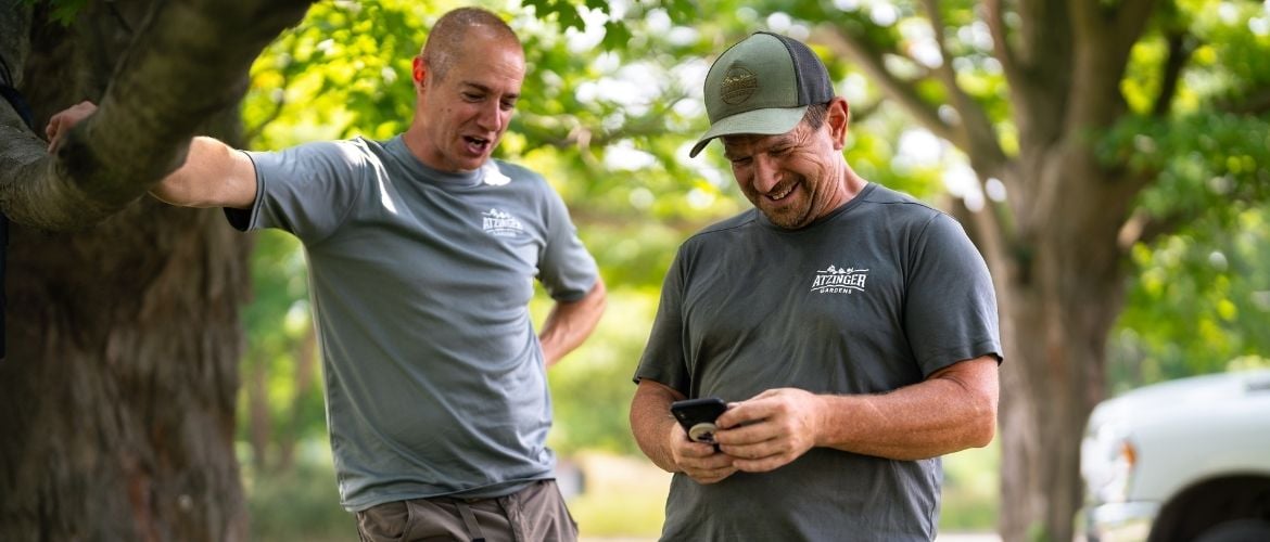 Two landscaping technicians on the job looking down at a mobile device