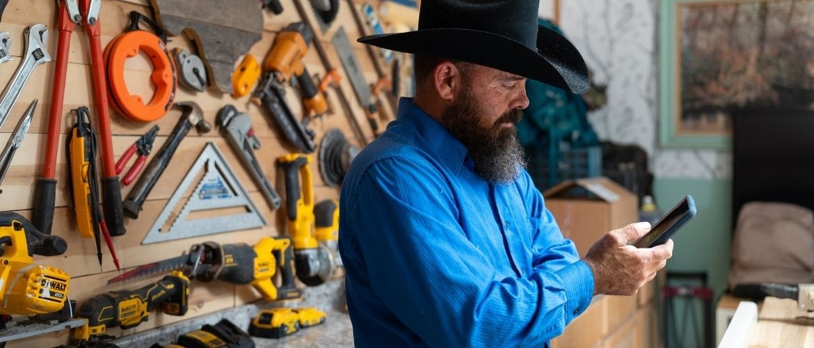 Handyman employee standing in front of a wall of tools looking down at their phone.