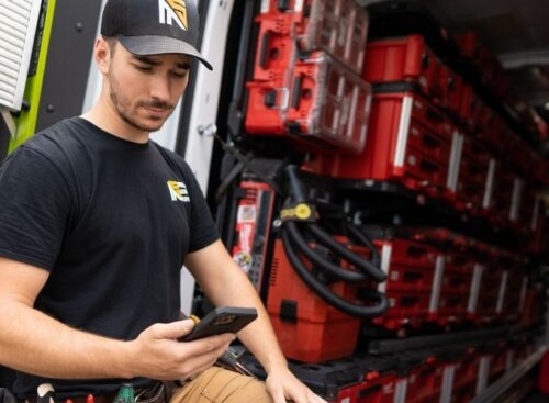 Electrician checking phone while sitting in a well-organized work van.