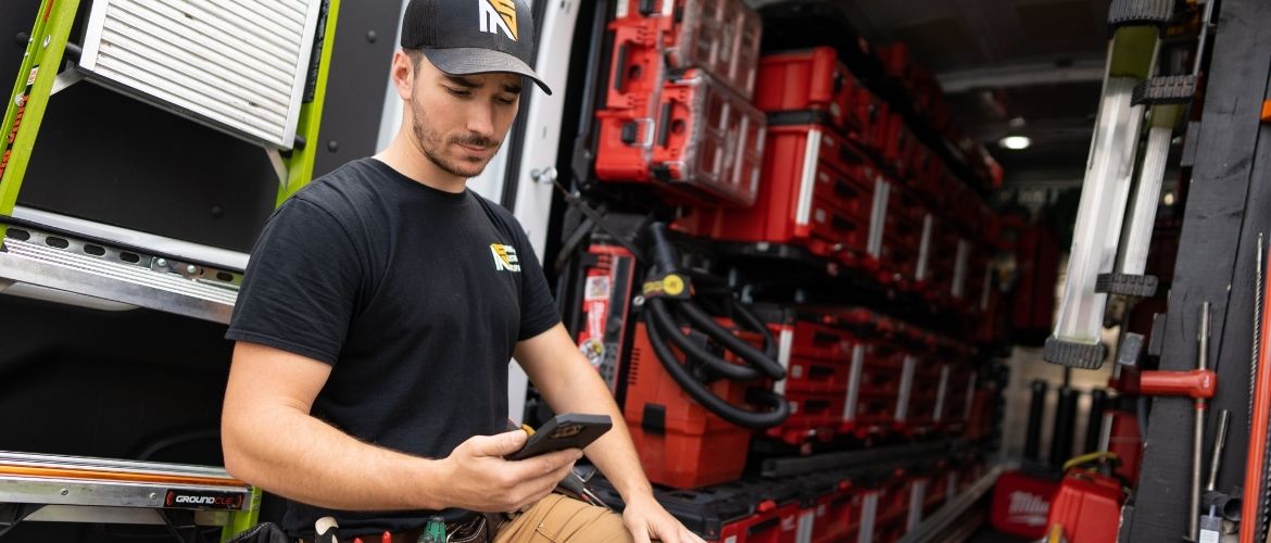 Electrician checking phone while sitting in a well-organized work van.