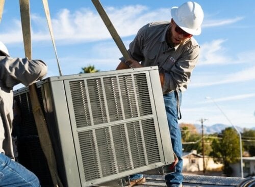 HVAC technicians installing a large air conditioning unit on a rooftop