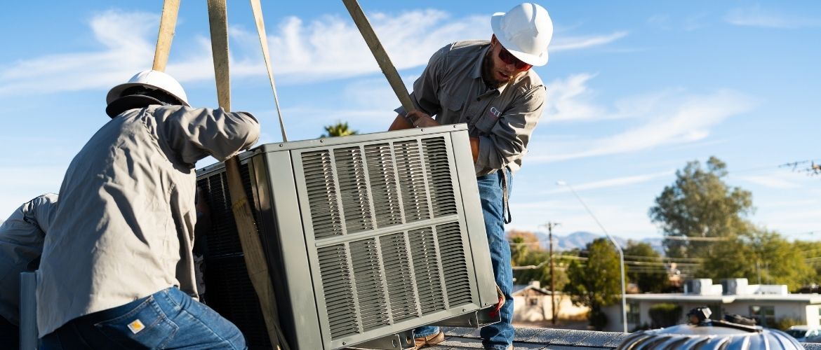 HVAC technicians installing a large air conditioning unit on a rooftop