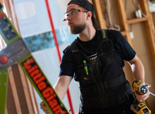 Contractor service provider holding a drill and ladder inside a building under renovation
