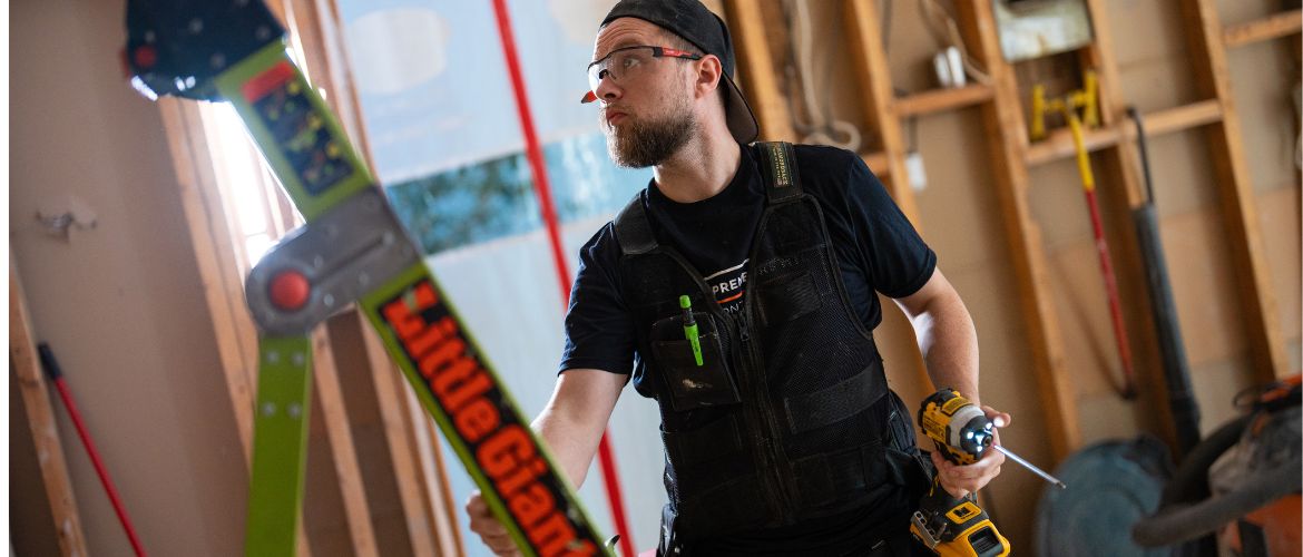 Contractor service provider holding a drill and ladder inside a building under renovation