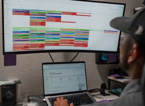 Person sitting at a desk using a laptop and a monitor displaying Jobber scheduling software