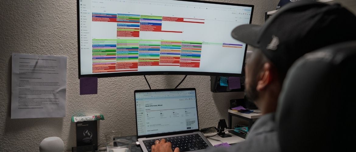Person sitting at a desk using a laptop and a monitor displaying Jobber scheduling software