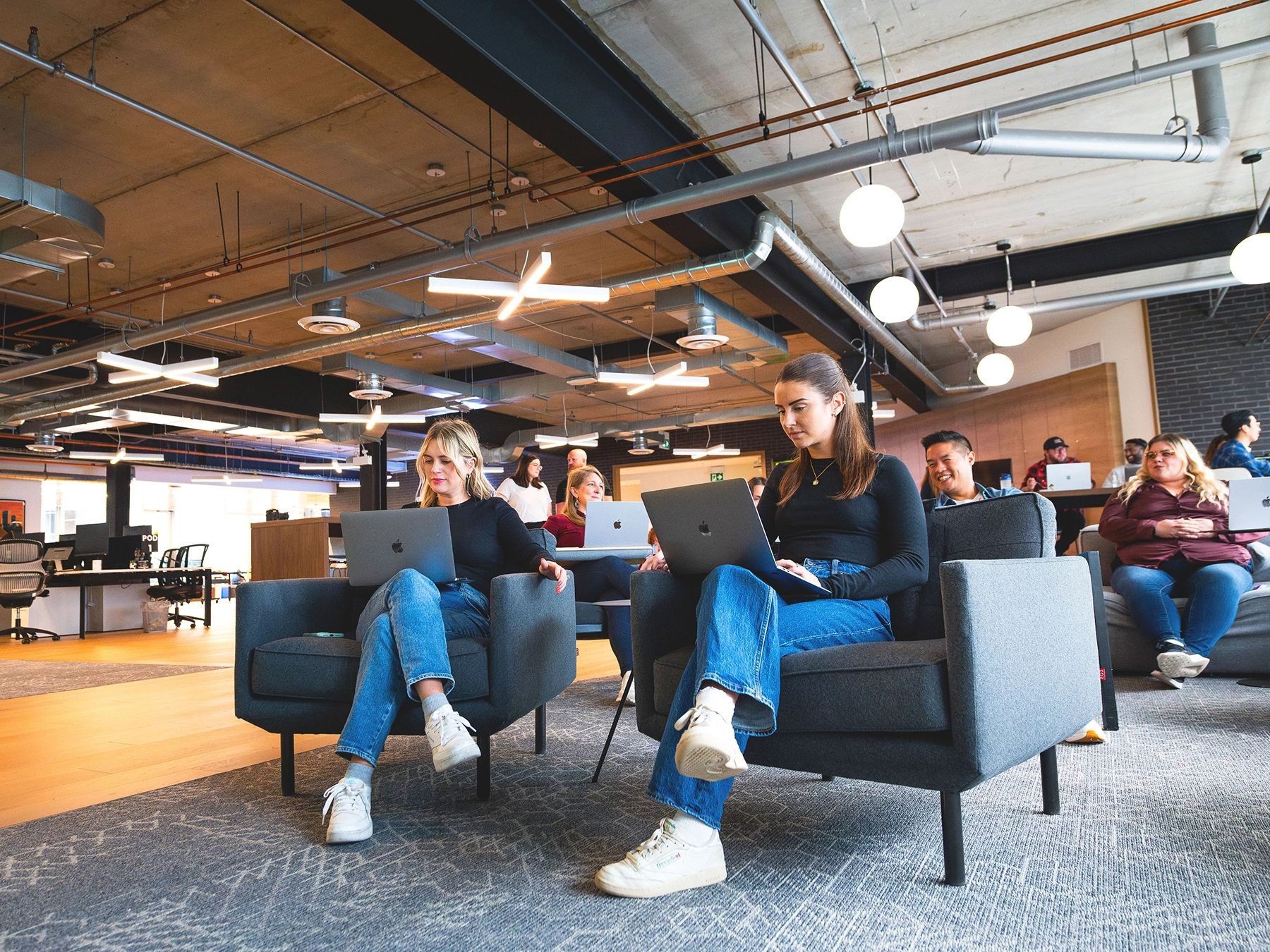 Two Jobber employees sitting on chairs with laptops.