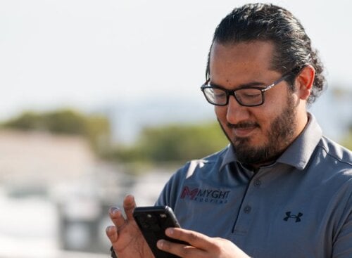 Image of a man in a Myght Roofing uniform looking at a cell phone.