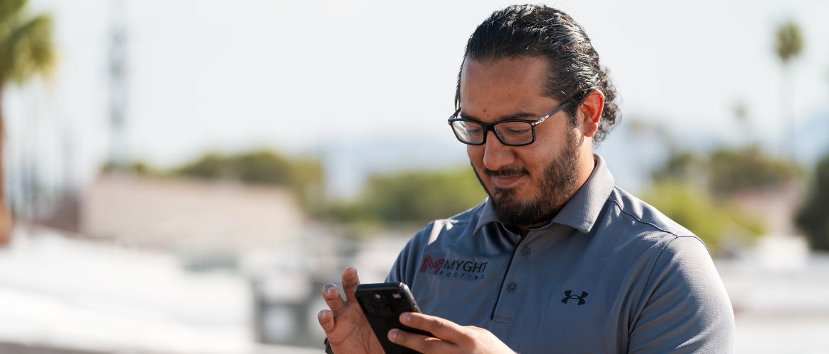Image of a man in a Myght Roofing uniform looking at a cell phone.
