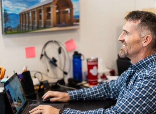 A franchise owner sits at a desk in a bright and busy office space, looking over a schedule on a monitor.