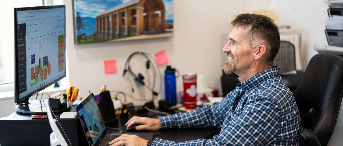 A franchise owner sits at a desk in a bright and busy office space, looking over a schedule on a monitor.