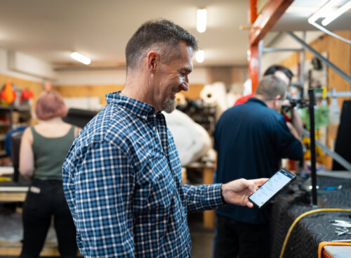 Image shows a franchise owner in a busy leather repair workshop, checking their phone while employees work on pieces in the background.