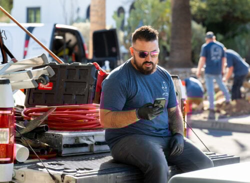 Plumber checking their phone while sitting on a truckbed at a jobsite