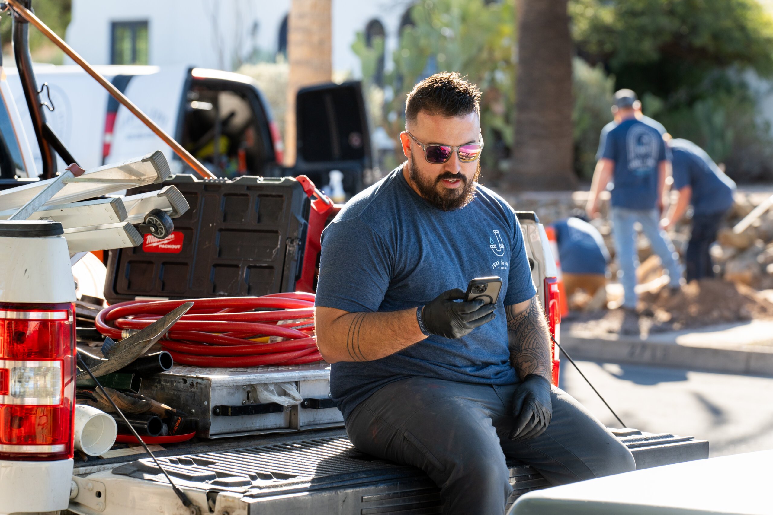 Plumber checking their phone while sitting on a truckbed at a jobsite