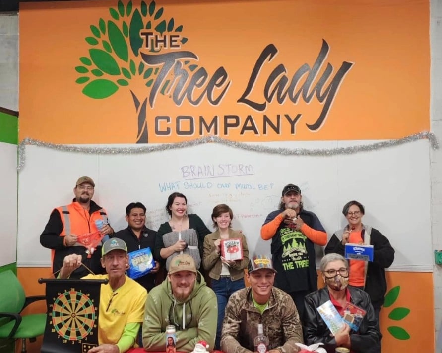 The Tree Lady Company team gathered indoors smiling and holding prizes during a team meeting.