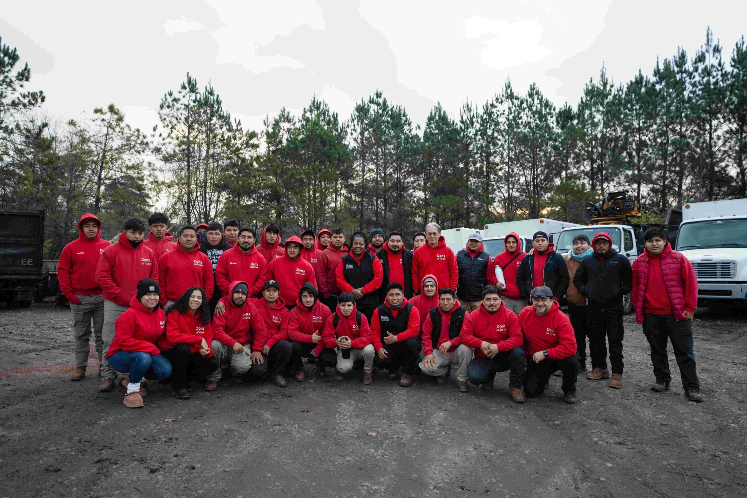 Don's Tree Service crew posing together in uniform in front of work trucks at a job site