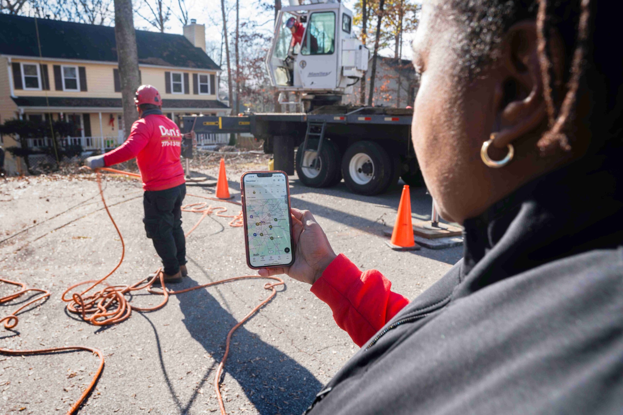 Crew member managing job routes on a phone while team works on a residential tree service job