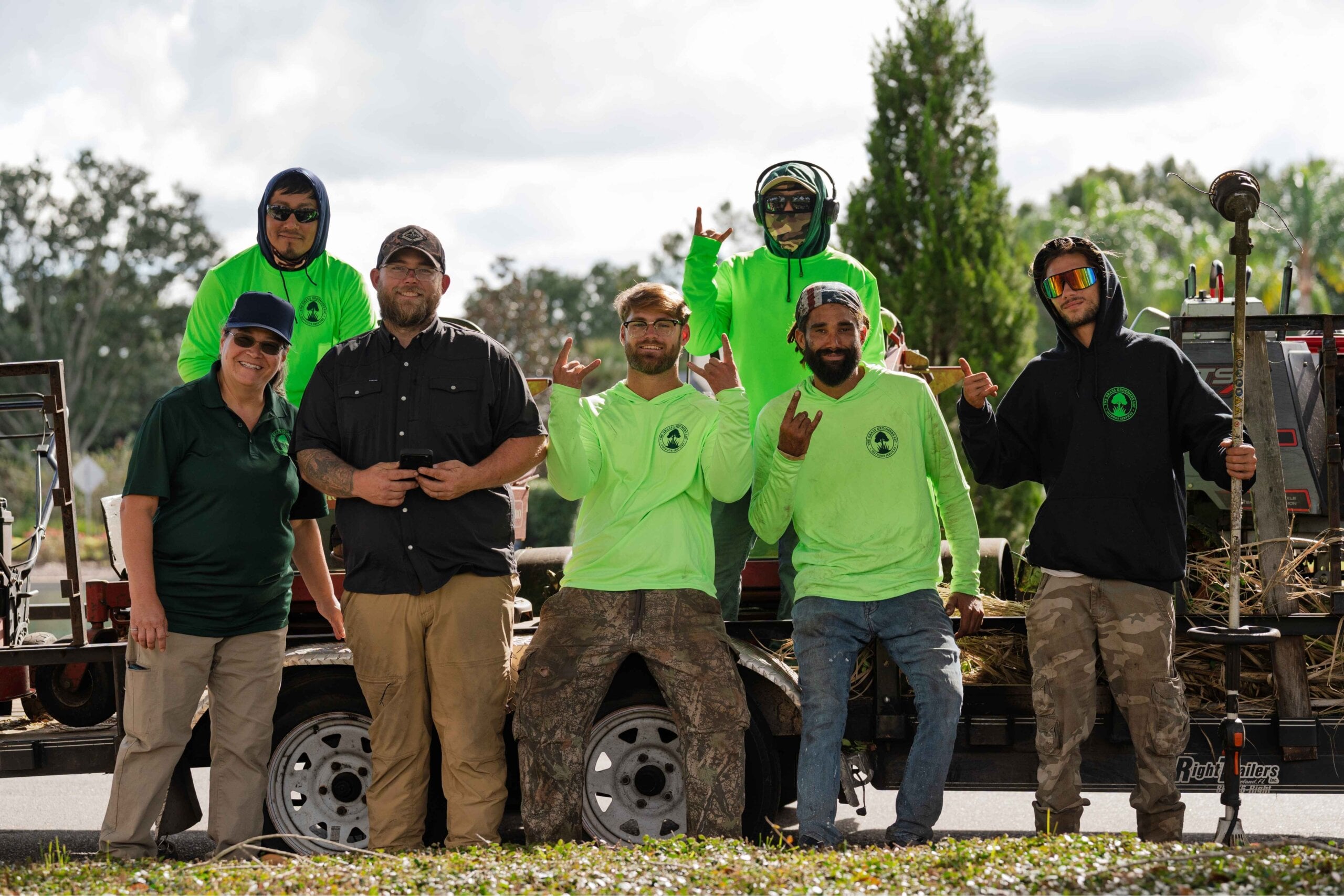 Grass Groomers crew posing together on equipment trailer at a job site
