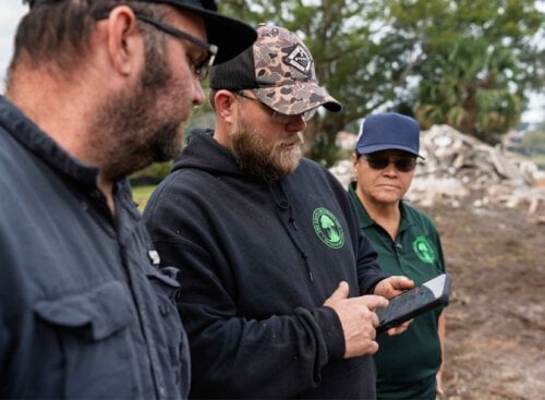 Grass Groomer team members reviewing job details on a mobile phone while standing together at a job site