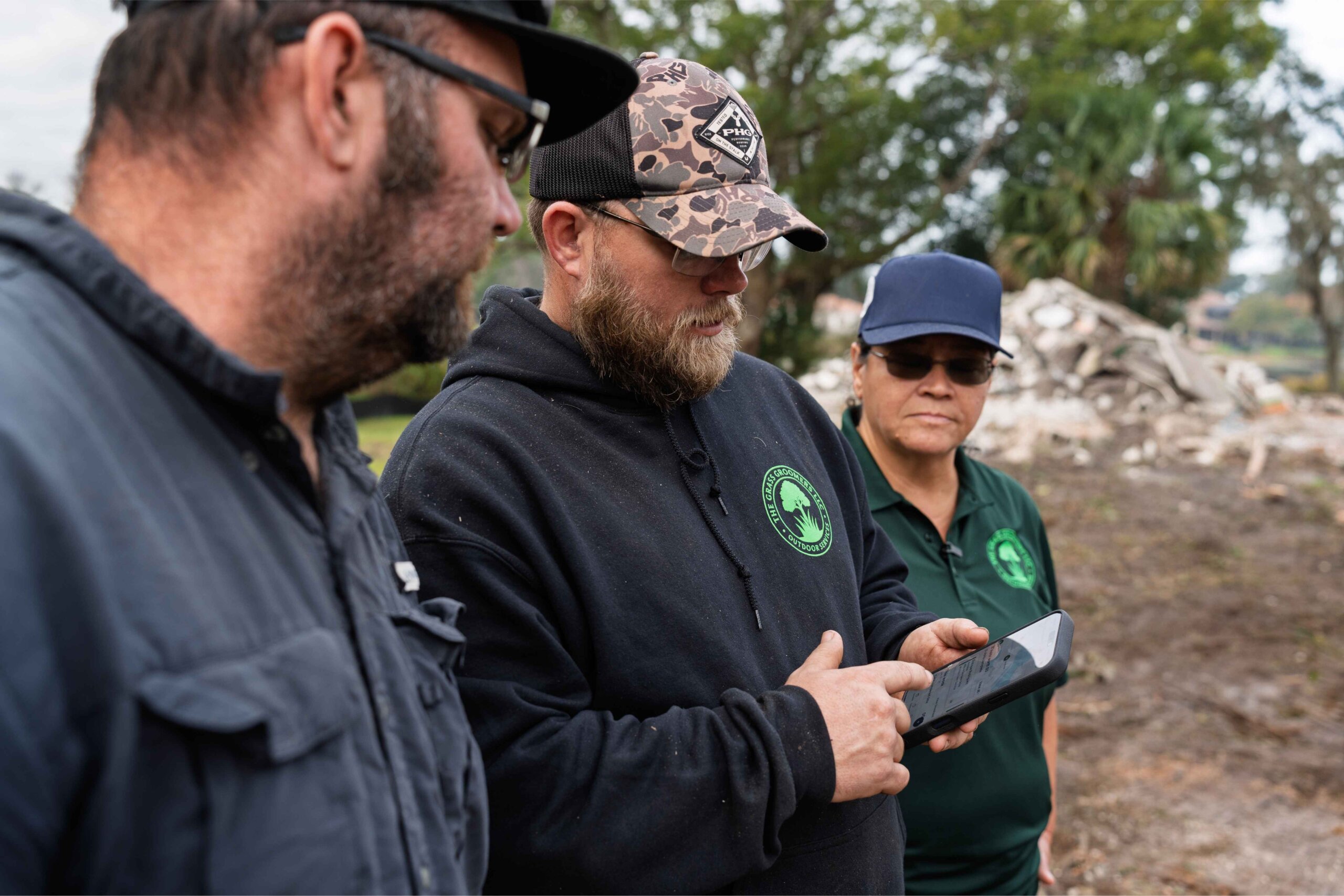 Grass Groomer team members reviewing job details on a mobile phone while standing together at a job site