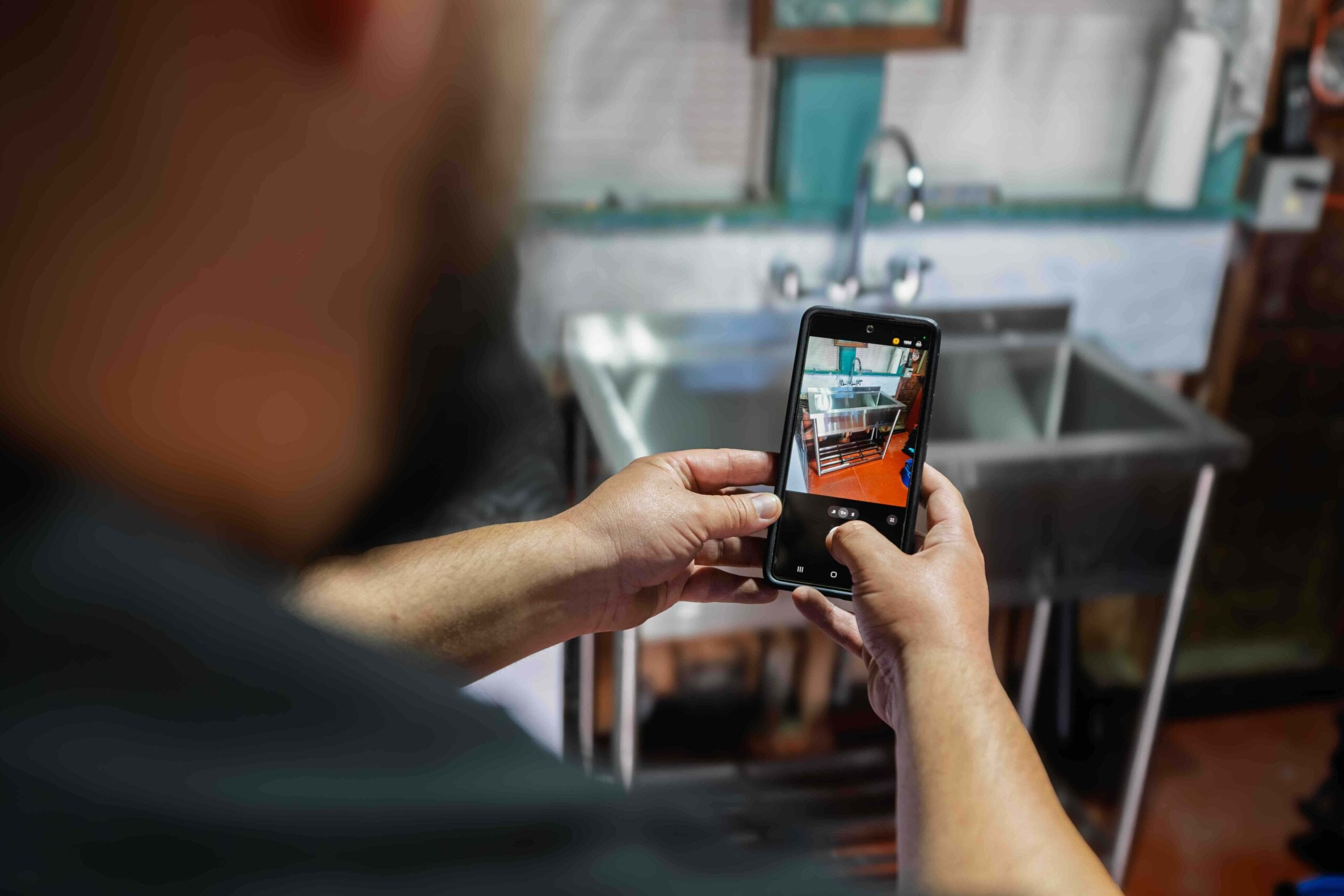 Frankie’s Plumbing technician uses a smartphone to photograph a sink during a plumbing inspection.