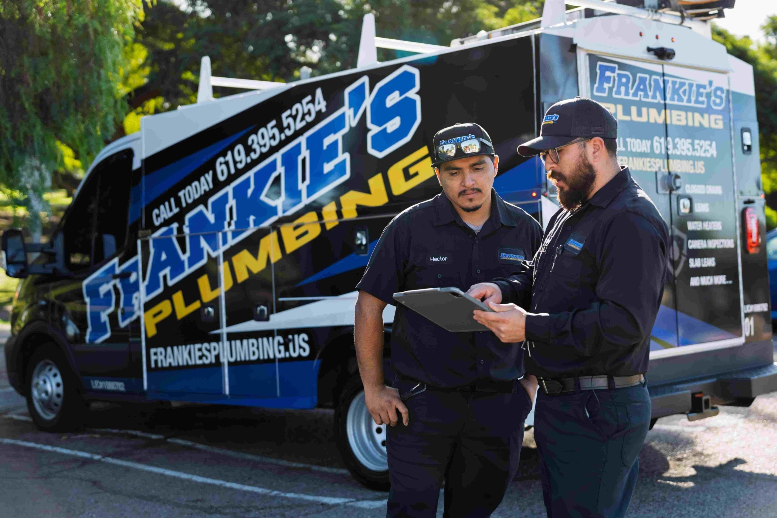 Frankie’s Plumbing technician and business owner review job information using Jobber’s mobile app beside a wrapped service vehicle.