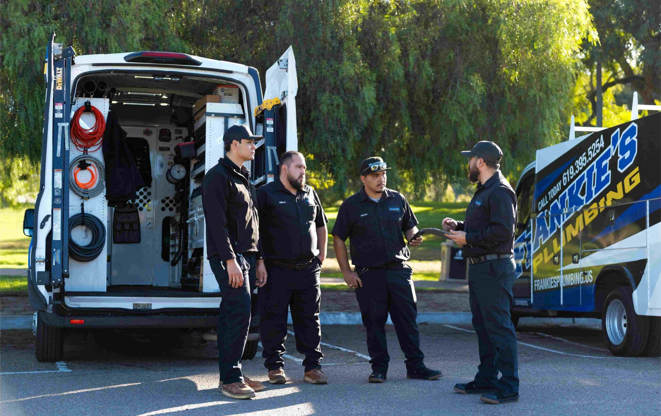 Frankie’s Plumbing technicians and business owner stand beside wrapped service vehicles discussing work.