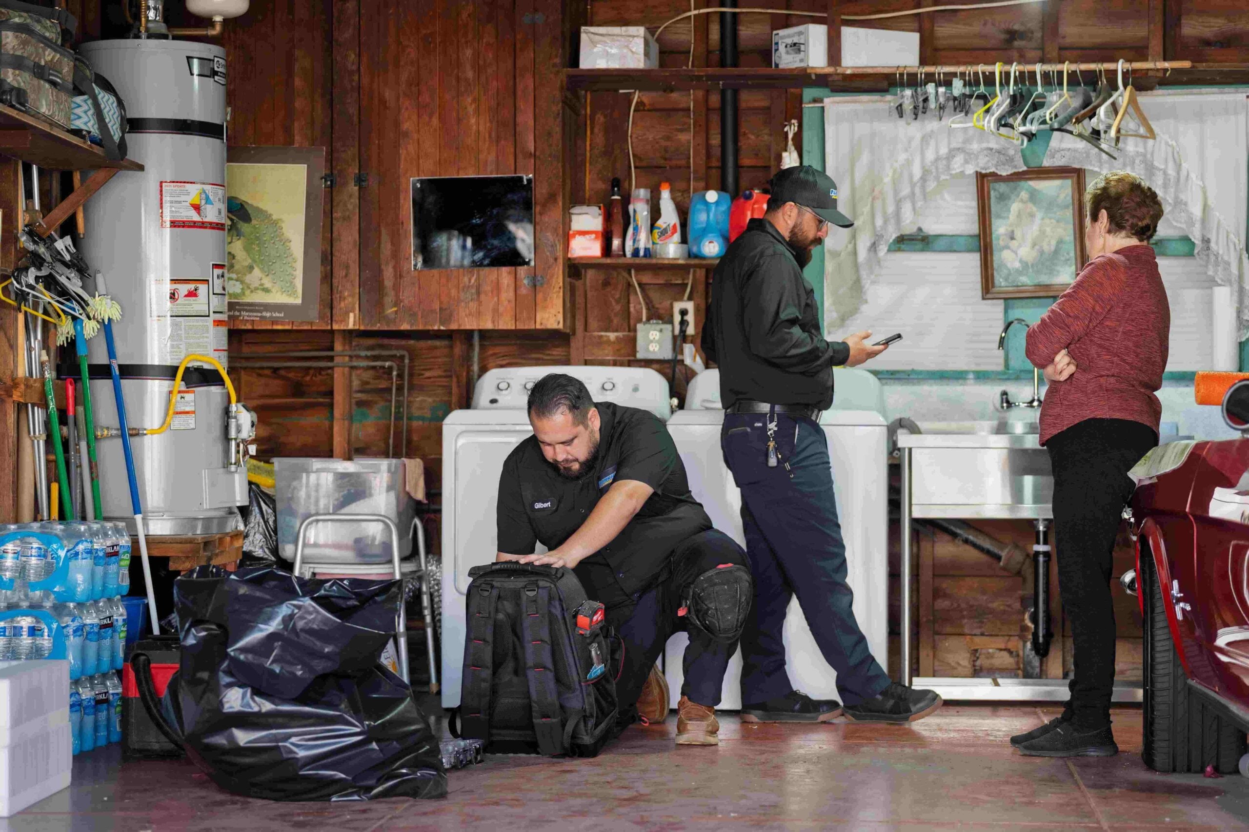 Frankie’s Plumbing team works in a garage while speaking with a homeowner during a service visit.