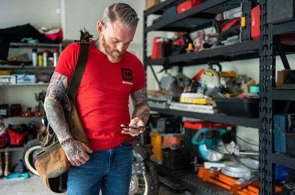 Service provider standing in a room with tools and equipment while looking down at his phone.