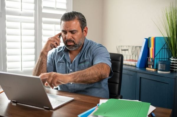A man sitting at his desk on his laptop while talking to someone on the phone